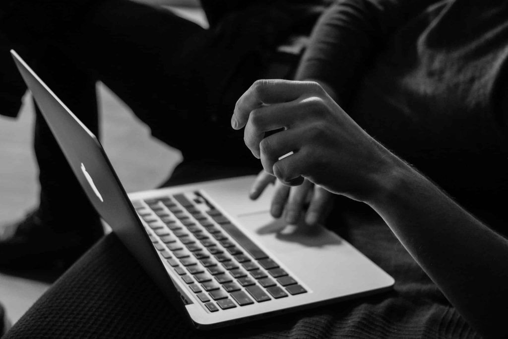 Black and white photo of a person using a laptop on a couch.