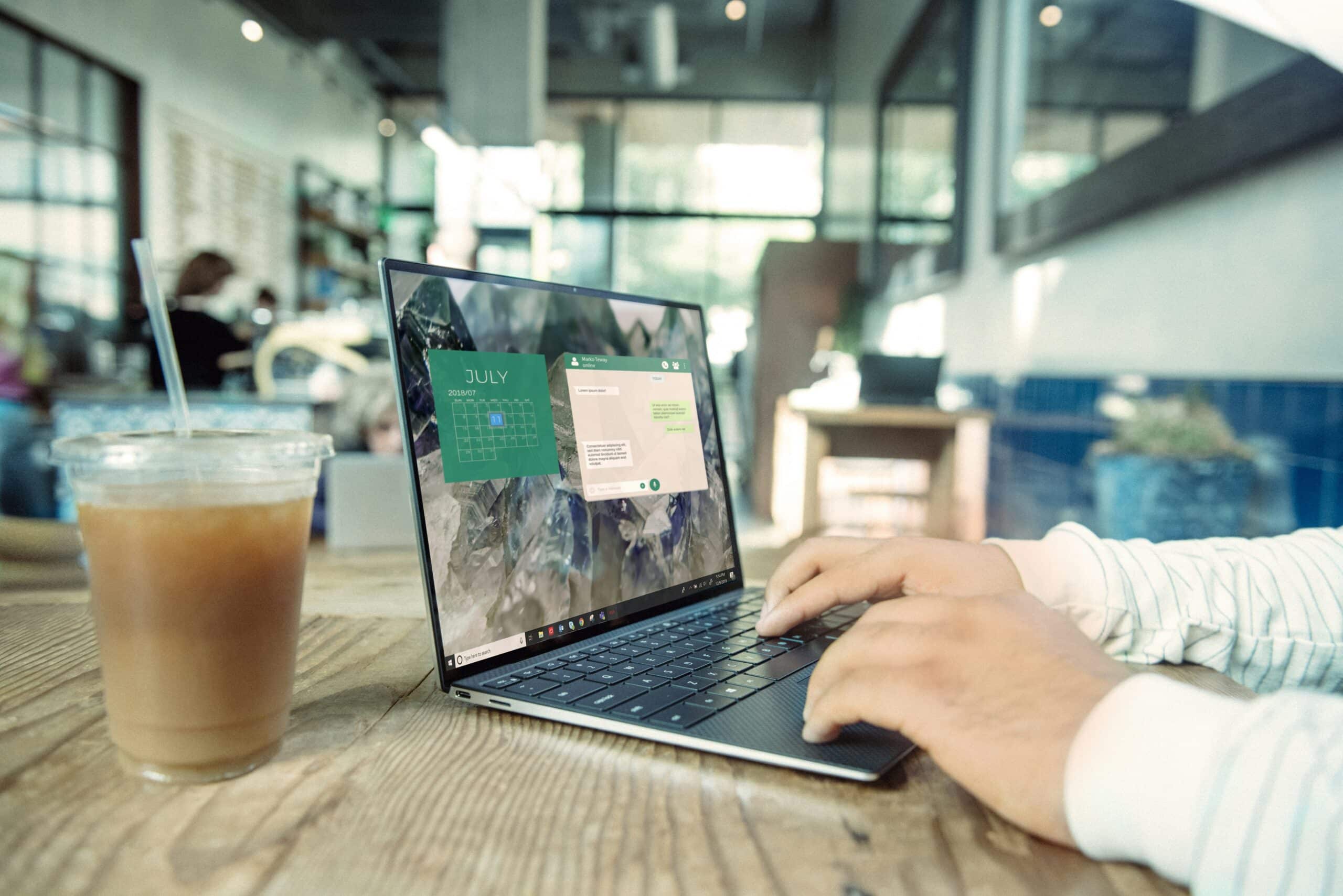 Person working on a laptop in a café with a digital calendar and notes interface visible on screen.