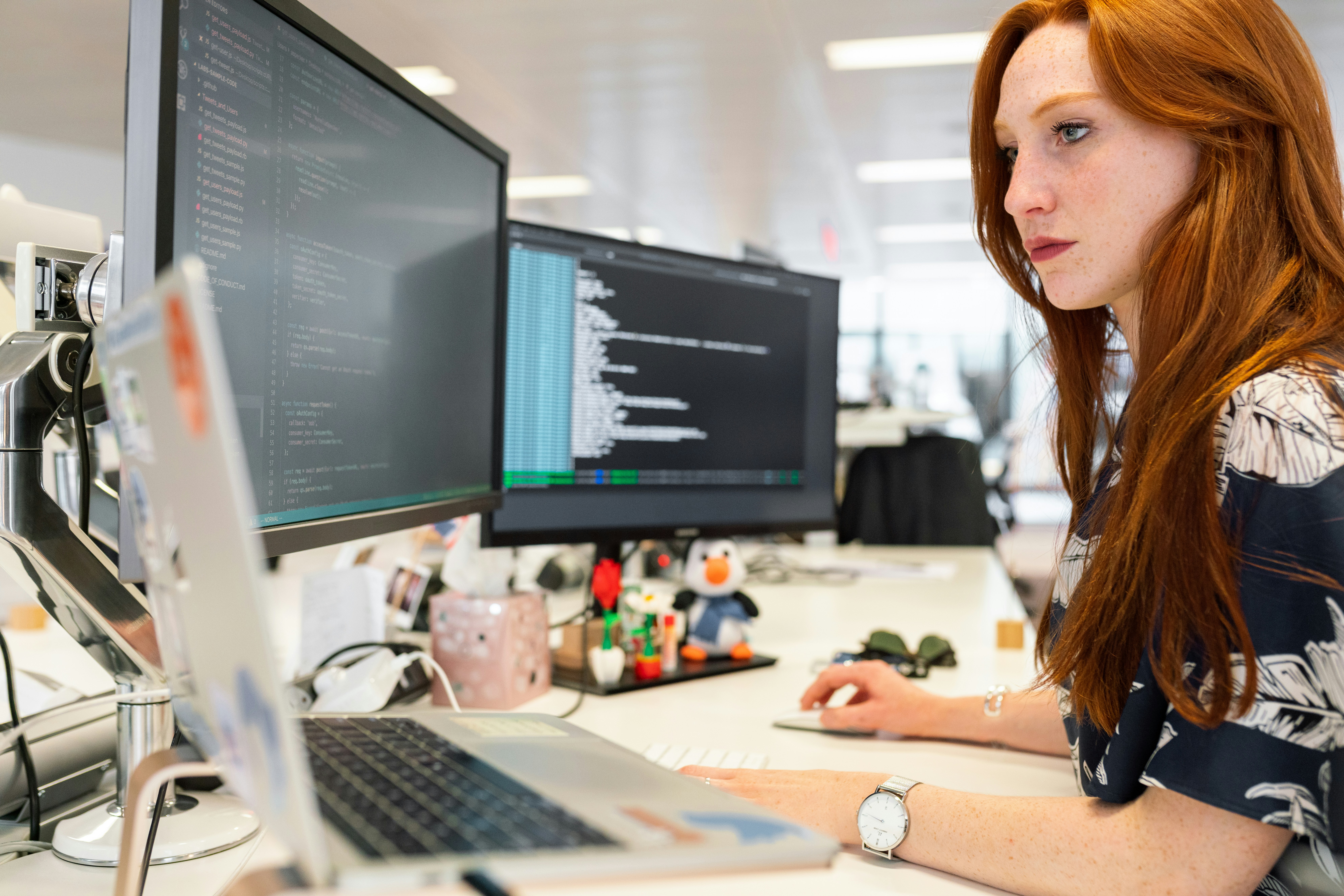 Woman working with dual monitors and code on screen